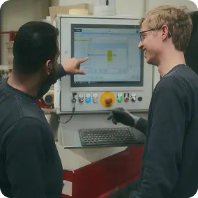 Zwei Mitarbeiter der Firma Keller & Wehbrink Möbelteile GmbH stehen vor einem Bildschirm und Besprechen die Produktion von Sockelleisten.